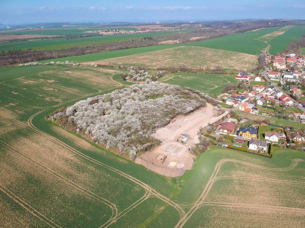 Vue aérienne : le verger en fleurs entouré de champs, le terrain du projet et le village à droite
